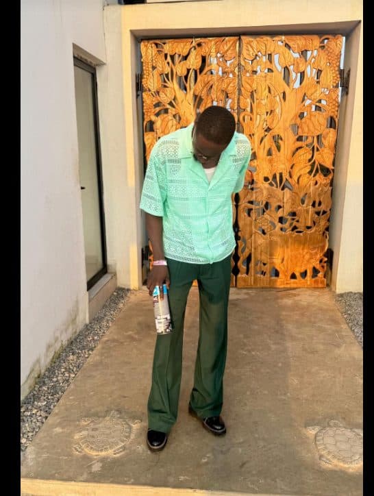 Mint green shirt and dark green trousers in front of a carved orange door